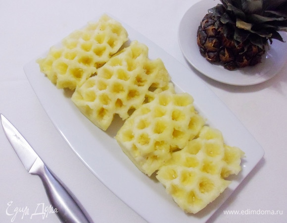 Очистить ананас. Срезать верхушку, потом — донышко. Затем срезать кожуру и вырезать «глазки». Разрезать ананас по вертикали пополам, затем каждую половинку — еще раз пополам. Вырезать жесткую сердцевину. Затем нарезать мякоть ананаса кусочками.