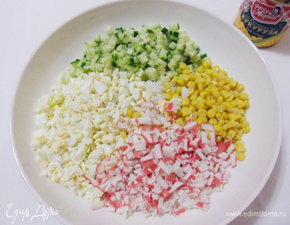 В миску выложить отварной рис, яйца, кукурузу, нарезанные огурец и крабовые палочки.