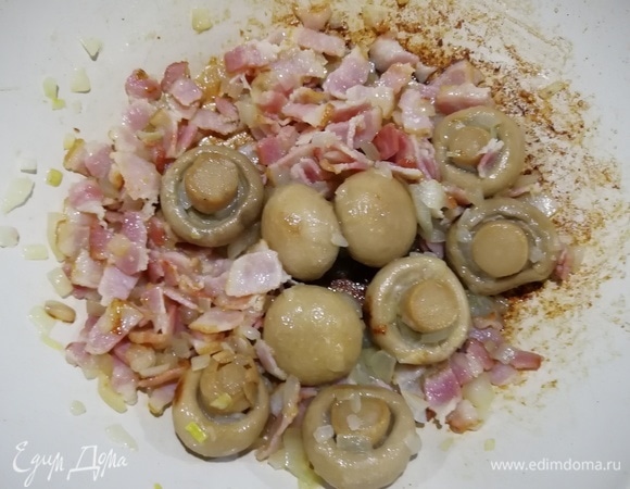 Добавляем к луку и бекону целые шампиньоны и обжариваем все вместе 5 минут. Я специально не режу грибы — так начинка получится сочнее.