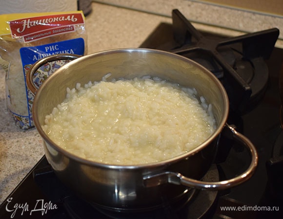 После этого уменьшить огонь и начать вливать горячий овощной бульон по одному половнику, постоянно помешивая рис. Следующий половник добавлять, только когда предыдущий впитался. Так продолжаем до желаемой степени готовности риса. Альденте — около 18 минут. Полностью готовый — 25 минут.