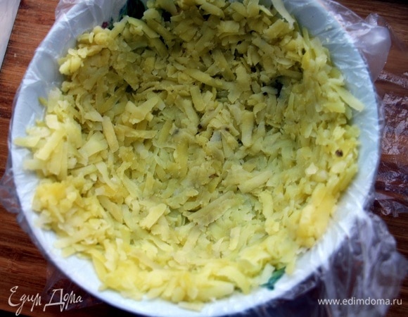 Дно тарелки застилаем пищевой пленкой. Натираем слой картофеля.
