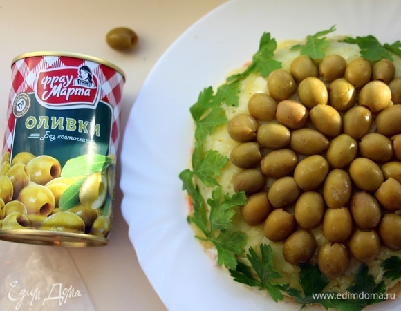 Далее аккуратно перевернуть салат на блюдо, снять пленку. Сверху украсить половинками оливок ТМ «Фрау Марта». Края салата украсить листиками петрушки.