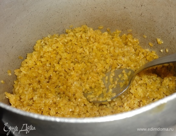 В другой кастрюле растопить сливочное масло. Выложить булгур ТМ «Националь», всыпать щепотку соли. Обжарить крупу в масле, помешивая.