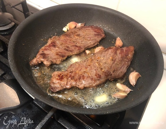 После того как перевернули мясо, добавляем на сковороду раздавленный чеснок и натираем им мясо, затем добавляем сливочное масло и розмарин (можно свежий, можно сушеный). С помощью ложки поливаем стейк содержимым сковороды.