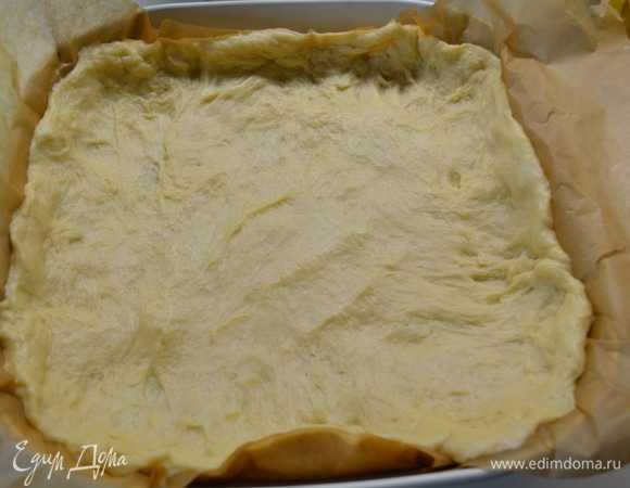 Форму диаметром 26 см выстелить бумагой для выпечки. Выложить тесто и разровнять по форме, формируя бортики.