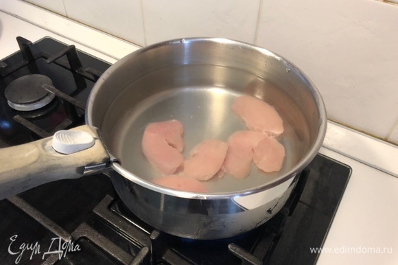 Выложите курицу в кастрюлю, залейте холодной водой. Доведите до кипения и снимите пену. Добавьте в кипящий бульон половинку очищенного лука и варите около 15–20 минут.