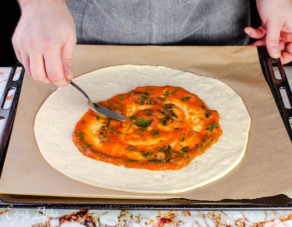 Раскатайте тесто в круг толщиной 1 см. Смажьте поверхность томатным соусом, а края — оливковым маслом.