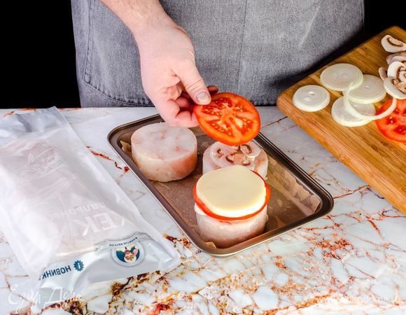 Разморозьте филе хека ТМ «Капитан Вкусов», посолите и поперчите. Застелите противень пергаментом, выложите рыбу, сверху – шампиньоны, лук, помидоры и моцареллу.