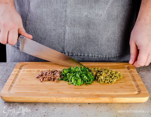 Измельчите кинзу, промойте и мелко нарежьте каперсы, анчоусы достаньте из масла и также измельчите.