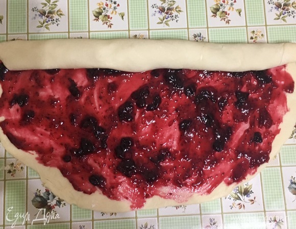 Когда тесто подошло, раскатать его в пласт, припылив мукой. Смазать начинкой, завернуть в рулет, края защипнуть.