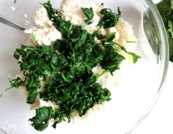 Нарезать мелко петрушку. Шпинат бланшировать 2–3 минуты, откинуть на сито, дать немного остыть, хорошо отжать руками, нарезать, добавить к начинке. Добавить петрушку.