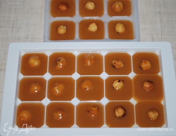 Формочки для льда смажьте растительным маслом и выложите в них карамельную массу, сверху положите по орешку. Уберите форму в морозильную камеру для застывания.