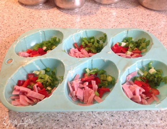 Силиконовую форму смазываю сливочным маслом. Выкладываю ветчину, лук, перец. Заливаю яичной смесью. Сверху щедро кладу сыр. Выпекаю 15–20 минут. Готовность зависит от возможностей вашей духовки. Так как яичной смеси в этом рецепте много, я пеку сразу два варианта (детский и взрослый). Взрослым — в керамической форме (керамическую форму также смазываю, выкладываю начинку, яичную смесь и сверху — сыр). Ставлю в духовку одновременно все формы.