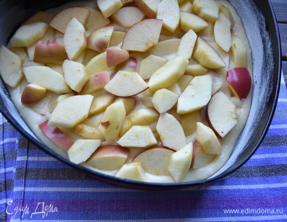 Форму для выпекания смазать маслом и слегка посыпать мукой. Остатки муки стряхнуть. Выложить половину теста. Сверху распределить нарезанные яблочные дольки.