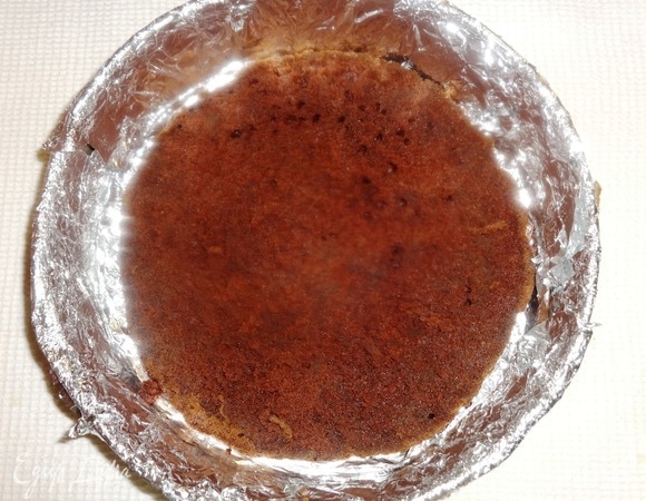 Разъемную форму полностью застелить фольгой, на дно выложить половину темного коржа.