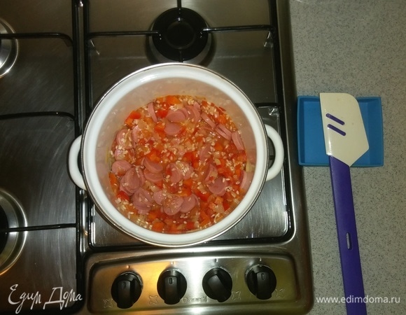 Затем добавляем сосиски. Опять все перемешиваем. И еще 5 минут продолжаем готовить овощи с рисом и сосисками на среднем огне.