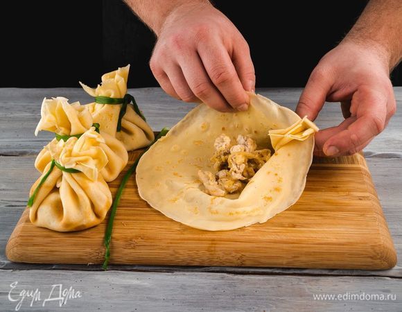 Готовые блины смажьте сливочным маслом, в центр каждого блина положите немного начинки. Аккуратно завяжите блинные мешочки перьями лука, опущенными в кипяток на 10 секунд для мягкости. Противень застелите бумагой для выпечки, положите на него блинные мешочки. Запекайте в духовке при 180°С в течение 10 минут.