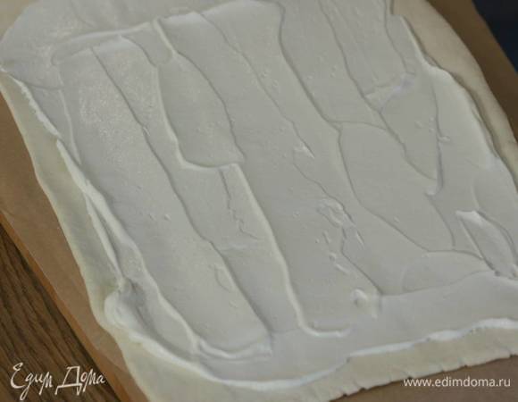 Тесто предварительно разморозить, затем слегка раскатать и смазать тонким слоем сметаны, немного отступая от краев.