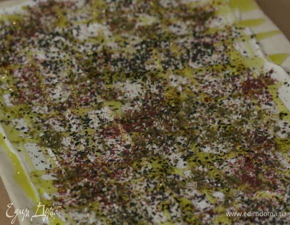 Посыпать лепешку со сметаной кунжутом, заатаром и сумахом, сбрызнуть оливковым маслом и свернуть в рулет.