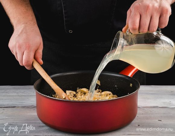 Влейте 200 мл бульона и тушите, постоянно помешивая. Продолжайте доливать бульон порциями, пока перловка не будет полностью готова.