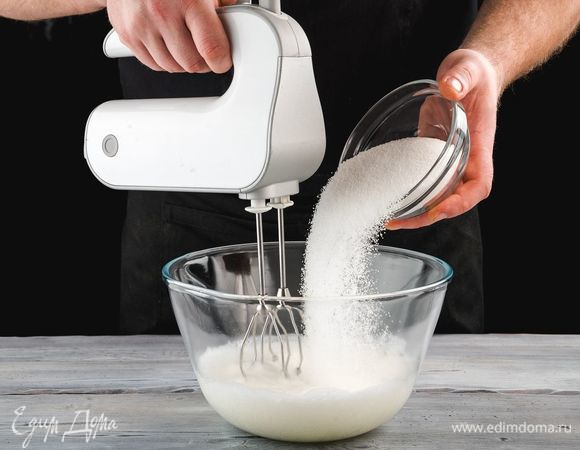 Приготовление пирожных начните с меренги. В чашу поместите яичные белки комнатной температуры и взбейте их миксером до появления мелких пузырьков. Постепенно всыпьте сахар в 3 захода, продолжая взбивать массу. Взбивайте белки до устойчивых пиков.