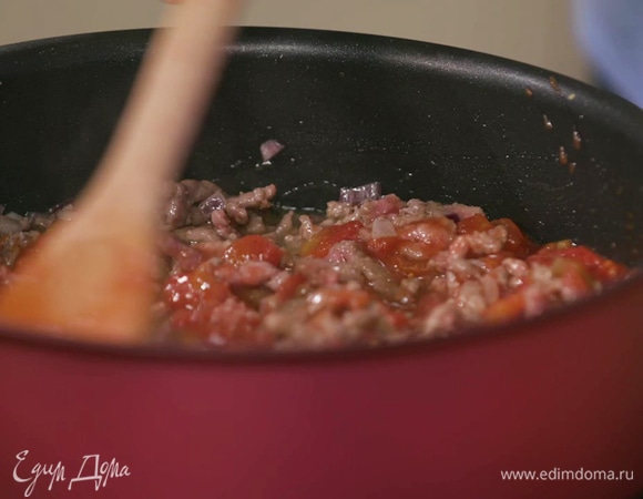 В сковороде разогреть оставшееся сливочное и оливковое масло и обжарить лук и чеснок, затем выложить фарш, посолить, поперчить, добавить оставшийся майоран, измельченные помидоры и все обжарить.