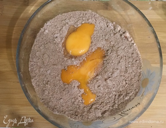 Добавить нарезанное на кусочки сливочное масло и измельчить до состояния крошки. Затем добавить желтки и перемешать.