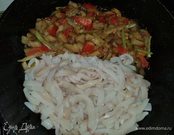 Сдвигаем овощи на одну половину сковороды, а на вторую выкладываем нарезанные соломкой кальмары и обжариваем минуты 3.