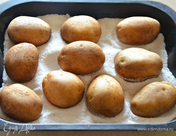 В глубокий противень насыпьте 1 пачку соли, разровняйте. Сверху равномерно распределите картофель.