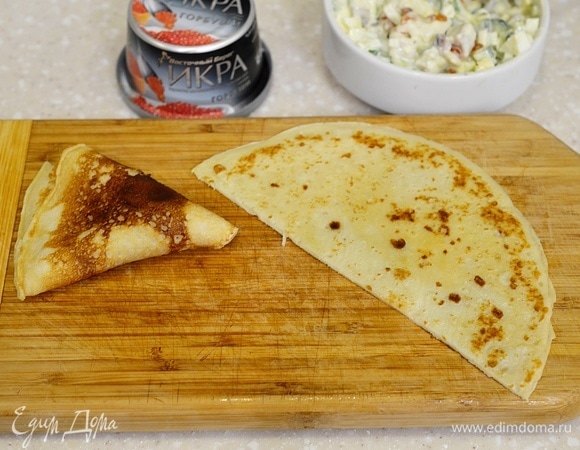 Каждый блин разрежьте пополам. Выложите немного салата и сверните кулечком.