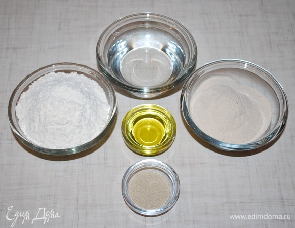 Два вида муки смешайте, насыпьте горкой, в середине сделайте углубление. Влейте в муку разведенные в теплой воде дрожжи, оливковое масло, посолите и заместите тесто.