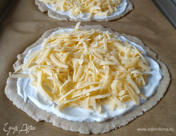 Сочни смажьте сметаной (или йогуртом) и посыпьте тертым сыром.