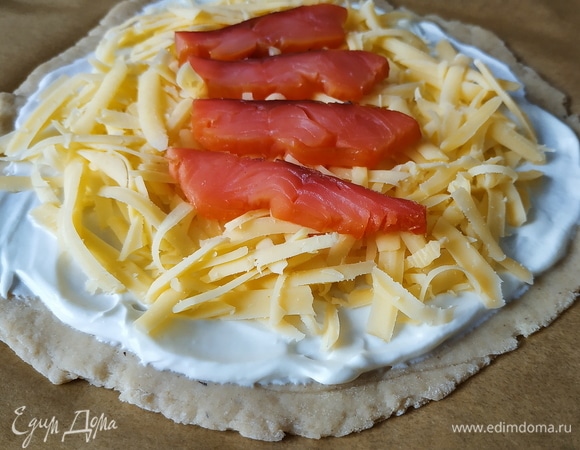 Сверху выложите нарезанные ломтики филе копченого лосося. Сверху можно полить оливковым маслом. Выпекайте пиццы в духовке примерно 20 минут при температуре 180°C до готовности.