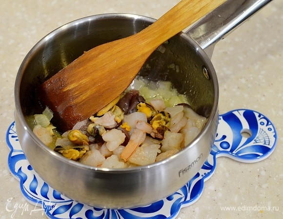 В сотейнике разогрейте масло, обжарьте лук. Добавьте морепродукты и обжарьте все вместе.