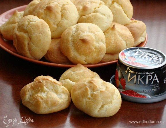 Тесто переложить в кондитерский мешок и отсадить профитроли на противень, застеленный бумагой для выпечки. Выпекать в разогретой до 200°C духовке сначала 5 минут, затем убавить температуру до 180°C и выпекать до румяного цвета минут 10–15.