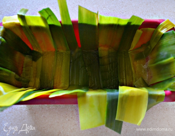 У лука-порея отрежьте зеленую часть, аккуратно раскройте и бланшируйте в кипящей, слегка подсоленной воде 1–2 минуты, после чего тут же охладите ледяной водой. Просушите листья порея с помощью бумажного полотенца и выложите в смазанную растительным маслом форму для кекса (края должны немного свисать).