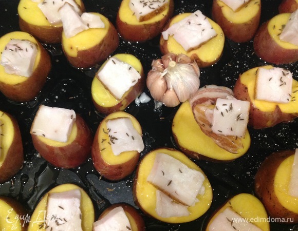 Разогреть духовку до 180°C. Сало или бекон нарезать на кусочки. Помыть картофель. Разрезать пополам, посолить, сверху положить кусочки сала или бекона. Противень смазать маслом, выложить картошку. Положить головку чеснока. Запекать картофель в духовке 30–40 минут.
