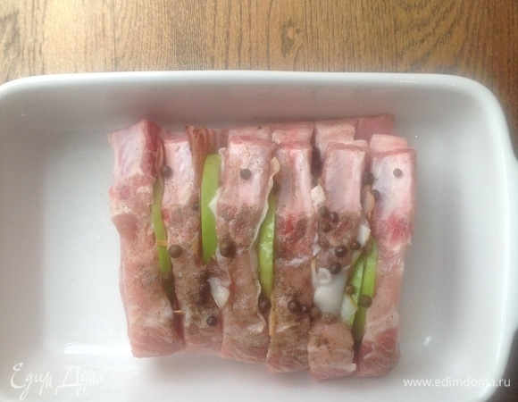 Духовку разогреть до 190°C. Корейку разрезать на порционные куски — прорезать не до конца. В ячейки положить по кусочку нарезанного яблока, затем — кусочек бекона. Скрепить мясо деревянными шпажками. Посолить, поперчить. Раздавить чеснок, смазать им хорошо мясо.