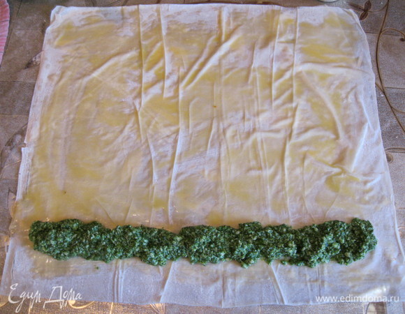 Если мы используем замороженный шпинат, то нагреваем его на сковородке с небольшим количеством растительного масла. Наша задача — испарить лишнюю жидкость, по консистенции он должен быть как зубная паста. Если шпинат свежий, то бланшировать в кипящей воде 1–2 минуты, хорошо отжать и нарезать. Включаем духовку на 190°C. В остывший шпинат добавляем натертый или просто размятый сыр, сырые яйца и перемешиваем. При необходимости досолить. Начинка готова! Тесто фило очень быстро заветривается и ломается, поэтому ту часть теста, с которой мы не работаем, накрываем влажным полотенцем. Теперь аккуратно отделяем листы теста фило, смазываем каждый растопленным маслом и на край выкладываем начинку, как на фото.