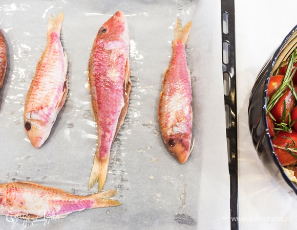 На противень стелим пергамент для запекания, легонько смазываем его оливковым маслом. Барабульку натираем солью и выкладываем на противень с пергаментом. 5 зубчиков чеснока мелко нарезаем, а остальные 5 оставляем для запекания. Помидоры режем пополам, смешиваем с измельченным и целым чесноком, солим, поперчим, добавляем 4 ст. л. оливкового масла, веточки розмарина и хорошо перемешиваем.