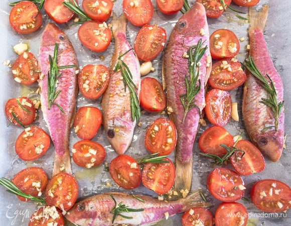 Выкладываем помидоры на противень, сверху поливаем соком от помидоров с чесноком и розмарином. Внутрь барабульки кладем мелко нарезанный чеснок — так она будет еще ароматнее. Запекаем в разогретой до 200°C духовке в течение 20 минут.