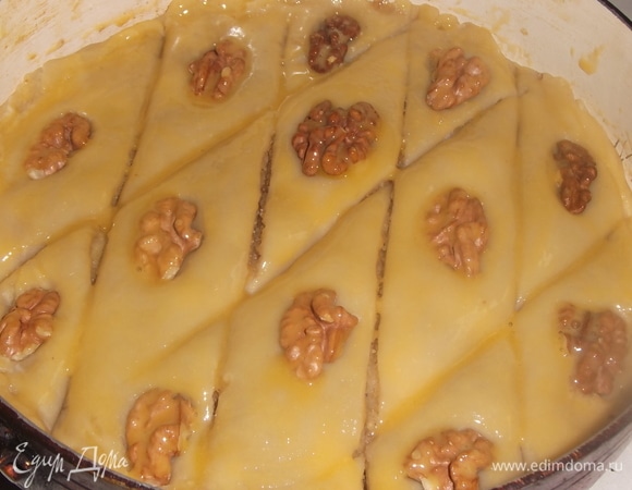 Выложить последний пласт теста. Соединить его с бортиками первого пласта. Надрезать пахлаву ромбиком, не дорезая до конца. Выложить сверху на каждый кусочек по ореху. Смазать желтком.