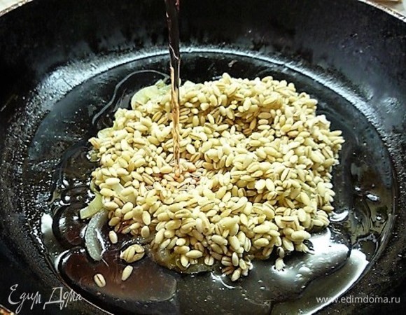 Добавляем перловку, перемешиваем, вливаем 50 мл вина и горячий бульон, накрываем крышкой и варим крупу до готовности (примерно 40 минут).