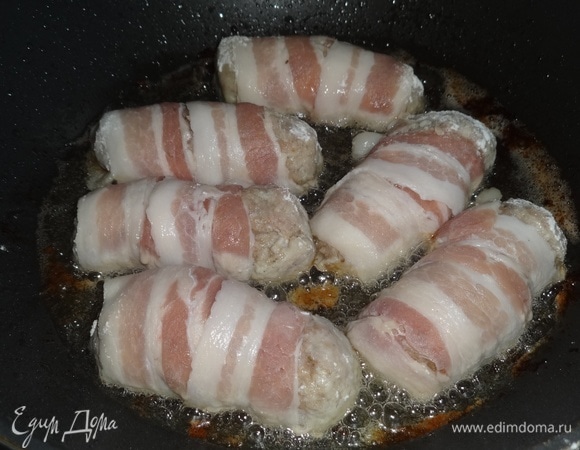 В сковороде разогреть растительное масло. Концы котлет, не закрытые беконом, обвалять в муке. Выложить котлеты в беконе на сковороду. Обжарить с одной стороны.