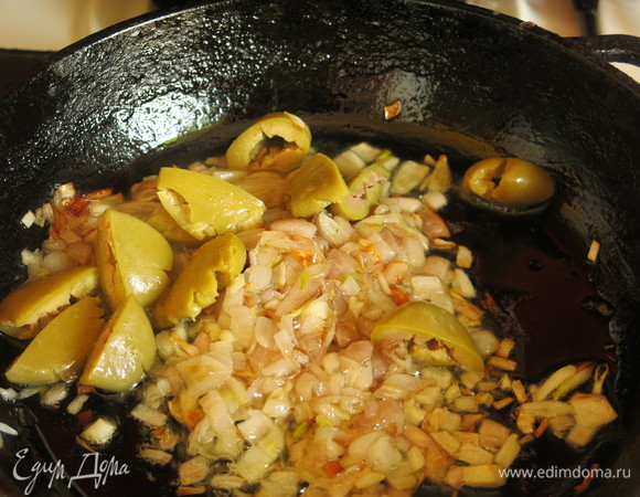 Если оливки с косточками, раздавливаем их и вынимаем косточки, кладем к луку. Обжариваем.