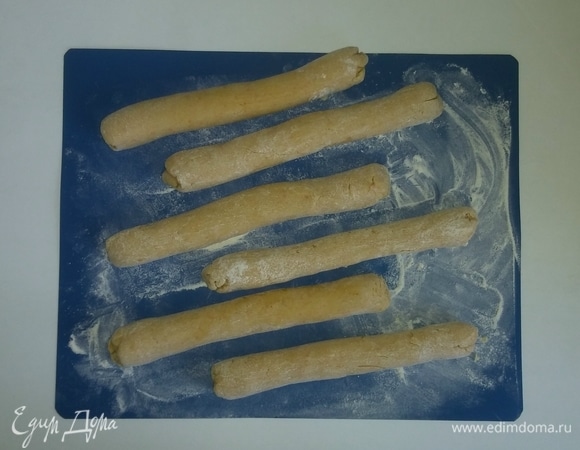 Поверхность для раскатывания посыпаем мукой. Отщипываем от теста кусок и скатываем из него колбаску диаметром 2–2,5 сантиметра и длинной 24 сантиметра (у меня форма для запекания 24×24 сантиметра). Из получившегося теста у меня получается 6 колбасок (если у вас форма для запекания больших размеров, то длину колбасок можно увеличить, но их будет меньше).