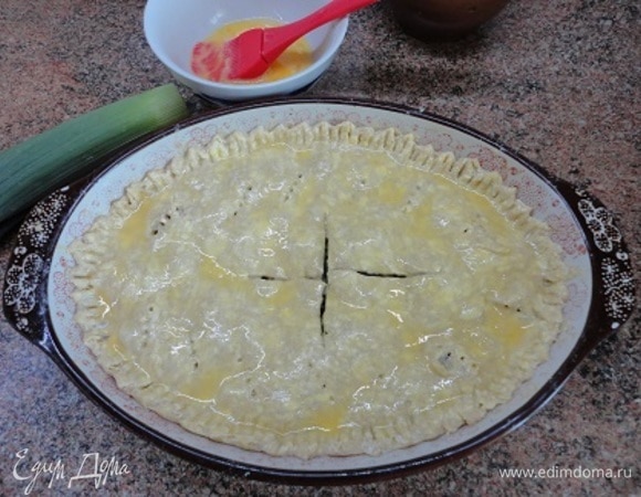 Накрыть вторым слоем теста, скрепить края, проткнуть тесто вилкой, а в центре сделать крестообразный надрез. Смазать яйцом и выпекать 50–55 минут при температуре 190°C.