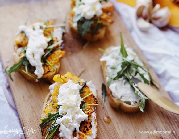 Сверху на сливочный сыр выложить запеченную тыкву. Затем — руколу. По желанию сверху можно выложить ломтики моцареллы или другого итальянского сливочного сыра.