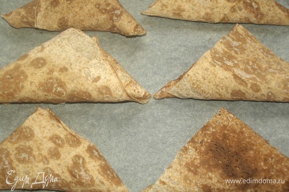 На застеленный пекарской бумагой противень кладем треугольники из лаваша. Отправляем в заранее разогретую до 180°C духовку на 7–10 минут.