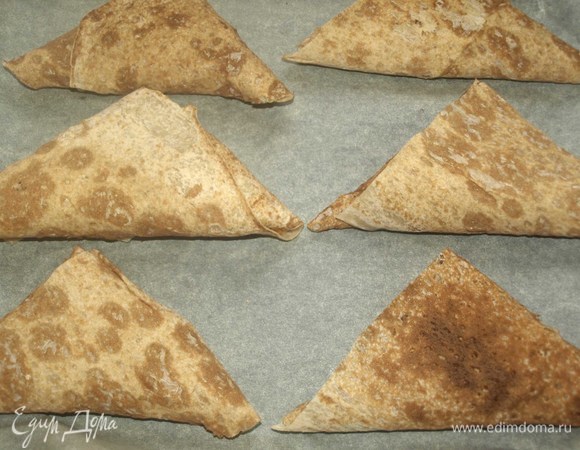 На застеленный пекарской бумагой противень кладем треугольники из лаваша. Отправляем в заранее разогретую до 180°C духовку на 7–10 минут.